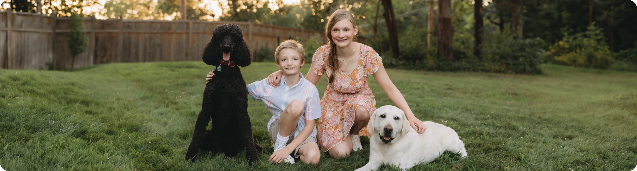 10:21 AMClaude responded: Two children kneeling in a grassy backyard at golden hour with two dogs—a black standard poodle and a yellow Labrador—beside them.Two children kneeling in a grassy backyard at golden hour with two dogs—a black standard poodle and a yellow Labrador—beside them.