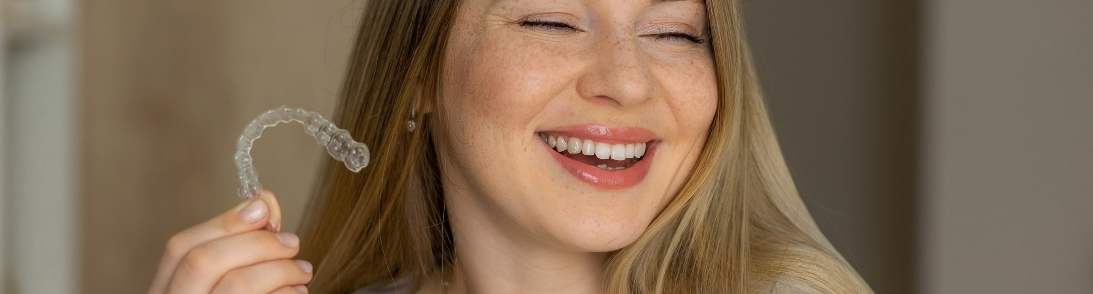 Woman smiles holding up her clear aligners at the orthodontist in Victoria MN